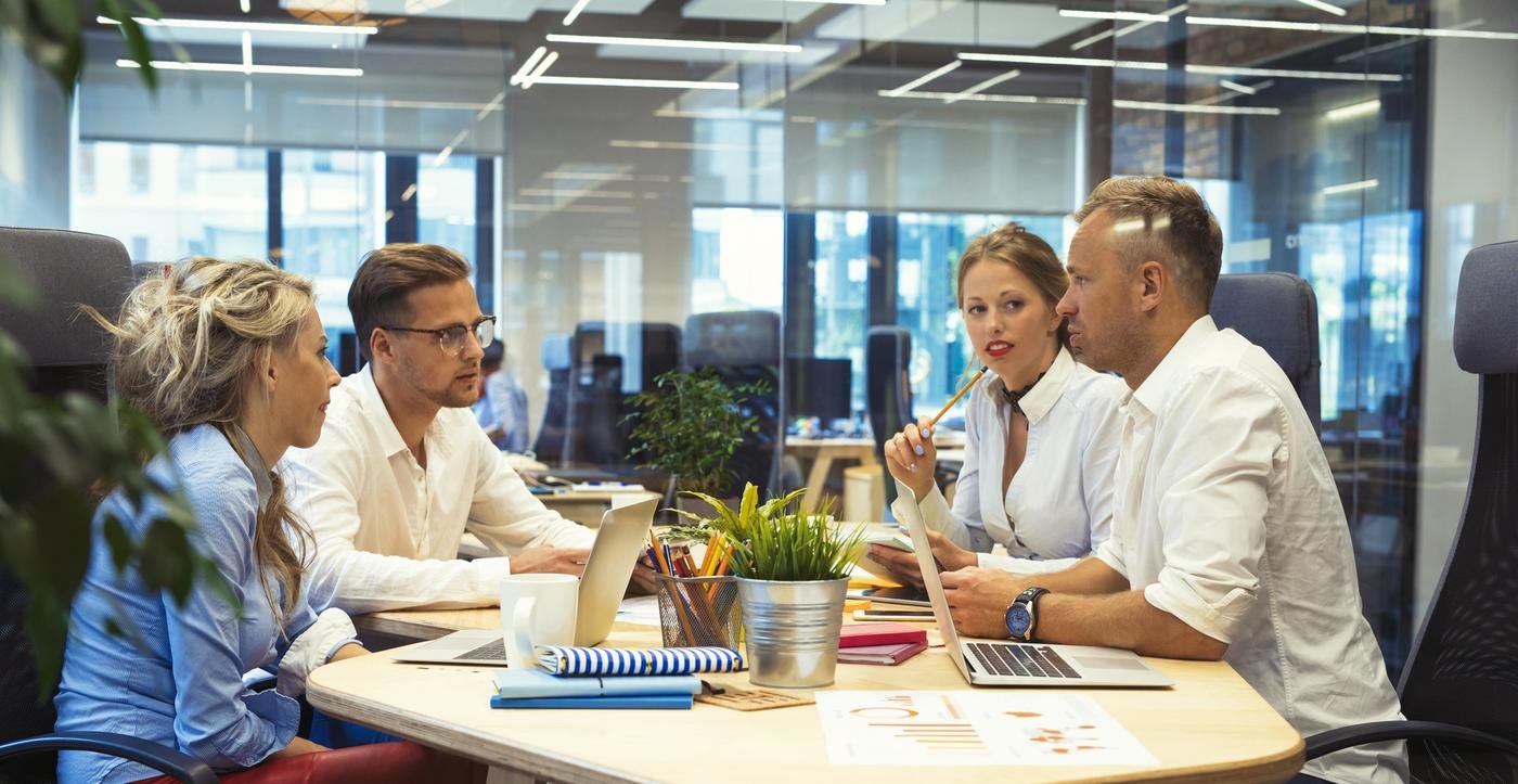 Dos mujeres y dos hombres trabajan en equipo en una mesa de una oficina diáfana.